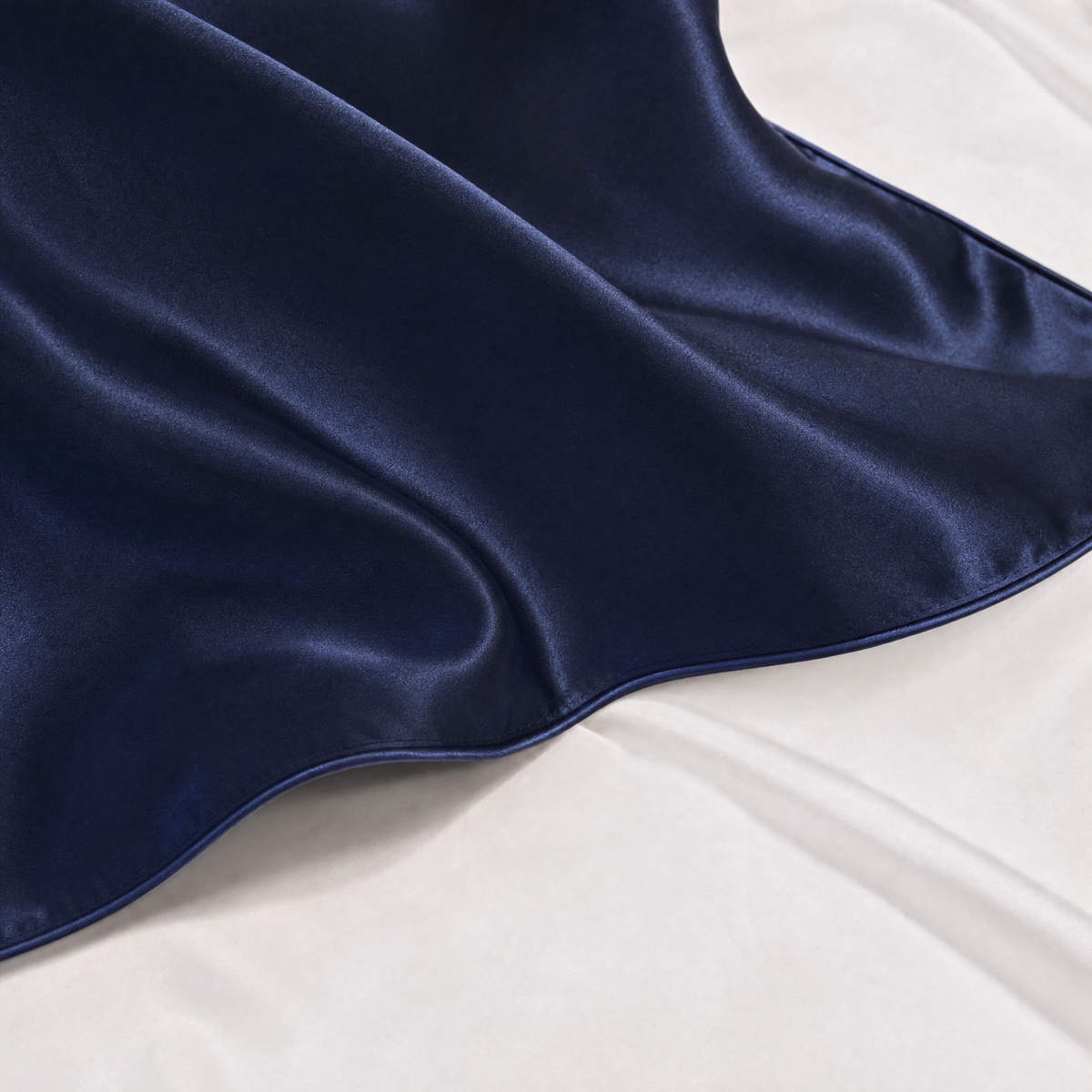 Close-up of Dark Blue mulberry silk pillowcase corner and piped seam on white bedding